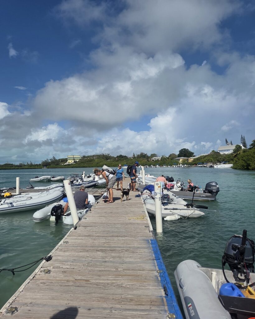 A wooden dinghy dock in the Bahamas lined with inflatable dinghies, under a big blue sky with white clouds.
