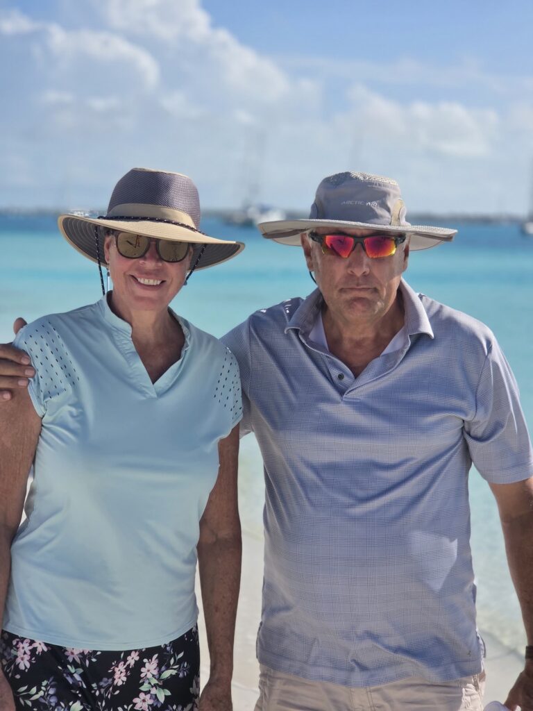Scott and Beth in sun hats on a white-sand beach with turquoise water behind