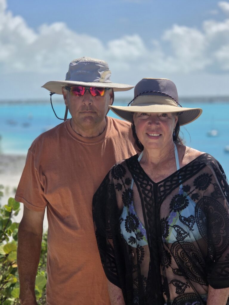 Scott and Beth in wide-brim hats posing above a bright blue harbor