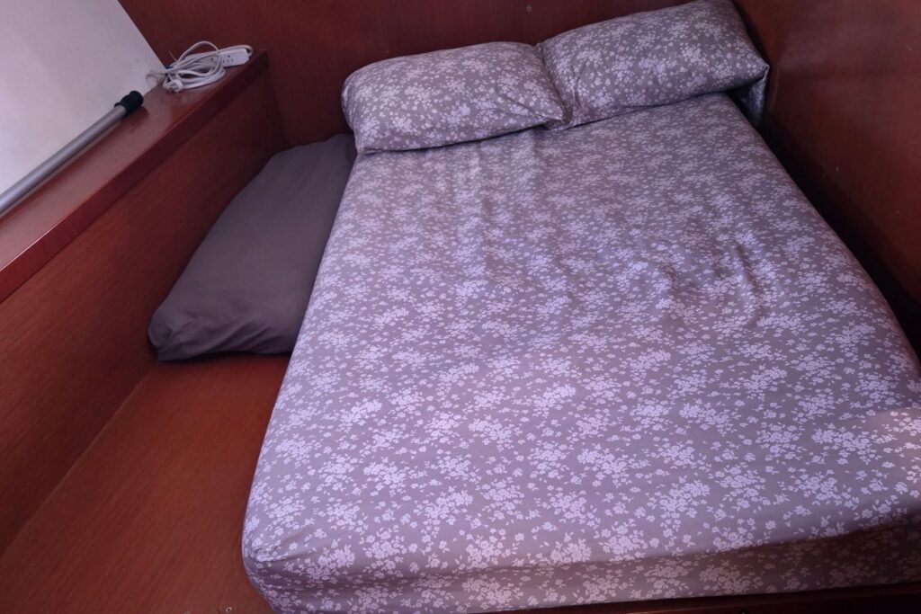 Starboard aft guest cabin with a double berth in gray floral bedding, warm wood paneling, and a teak-look floor.